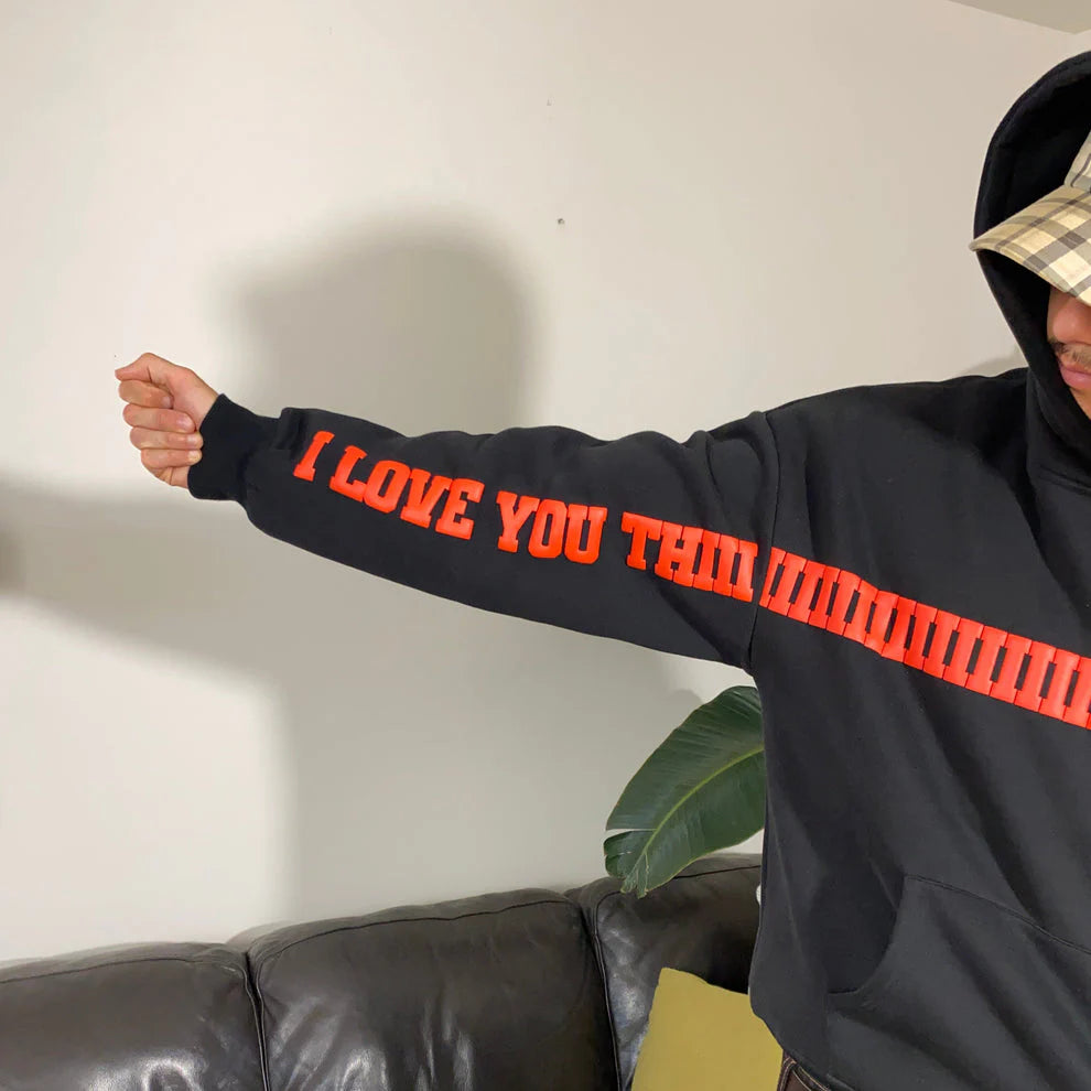 Model wearing black oversized hoodie with “I LOVE YOU THIS MUCH” printed on the front